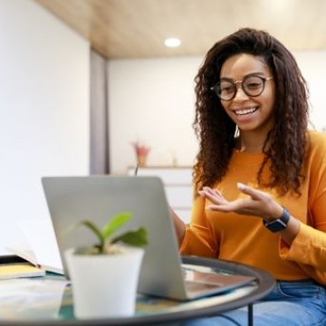Foto van een vrouw met een bril. Ze kijkt blij en gebaart naar haar laptop.