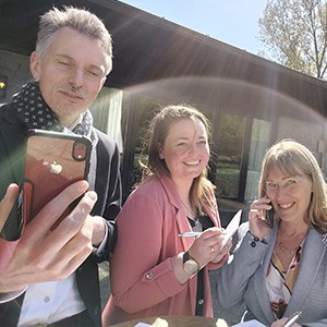 Een foto van drie collega's. Eentje maakt een foto, de ander belt en de ander noteert.